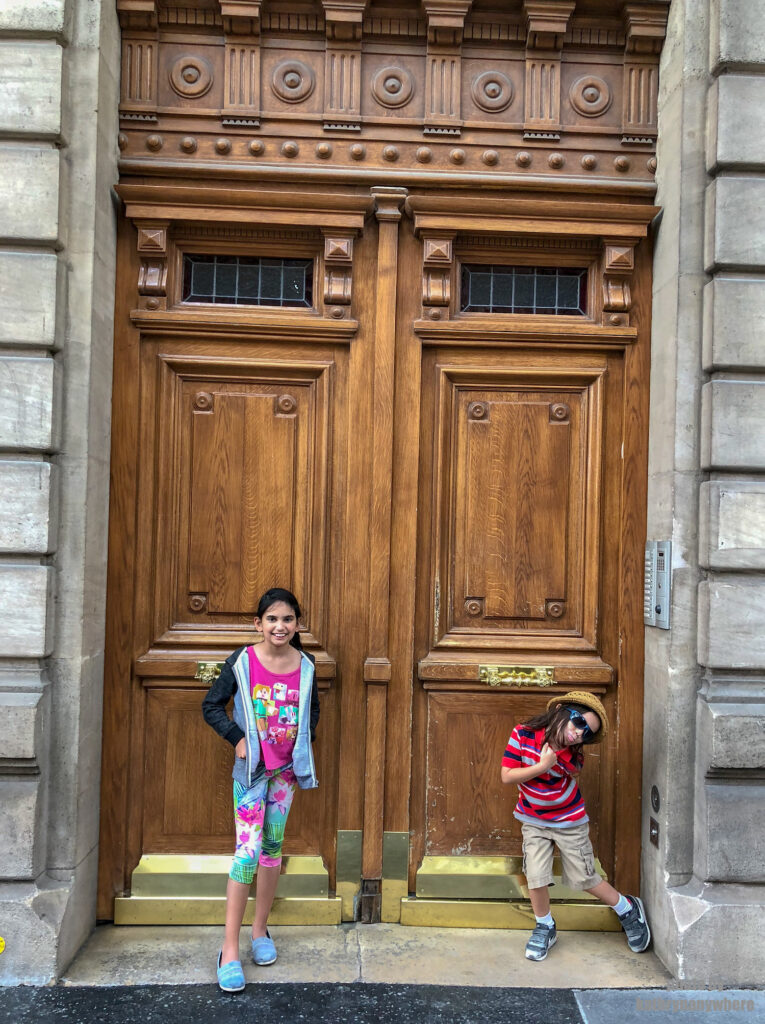 Short, brown, wooden door with windows at the top in Paris. This picture with my children was taken in 7th arrondissement neighbourhood in Paris, France