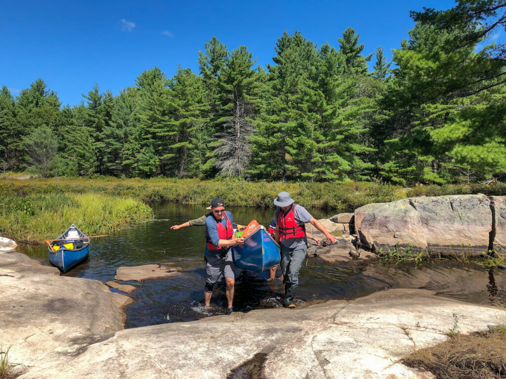 A couple men carrying a canoe over rocks in Kawartha Highlands provincial park