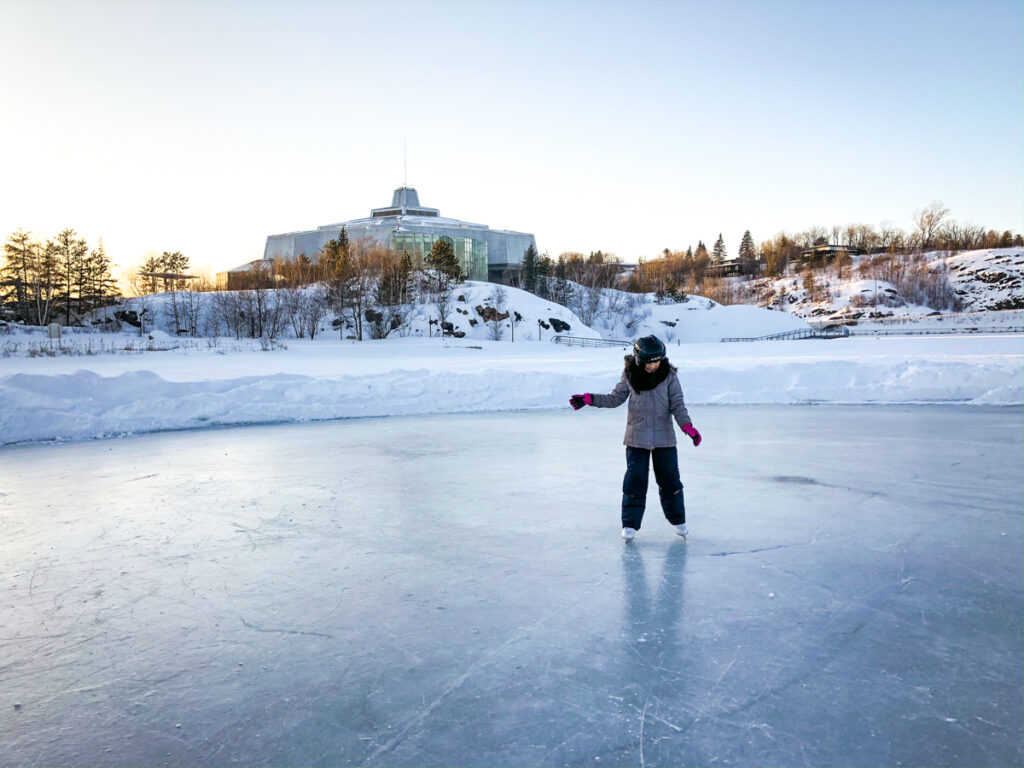 Sudbury Winter Activities young girl skating on Ramsey Lake with Science North in the background
