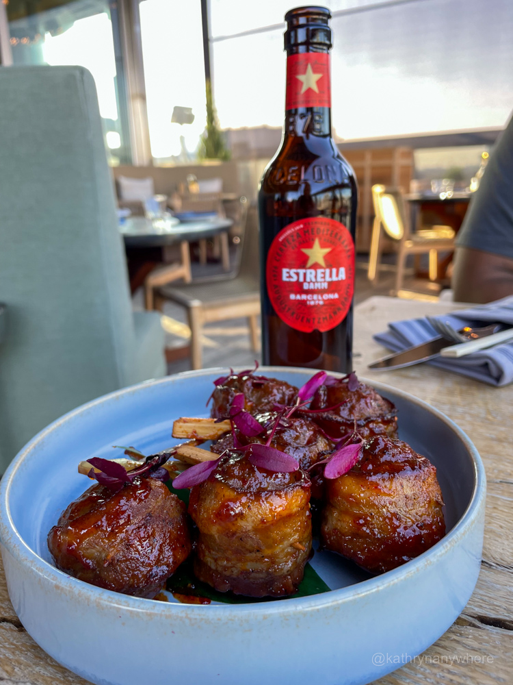 Food is Beef Tsukune and Estrella Damm bottle of beer at Harriet's Rooftop Patio in Toronto.
