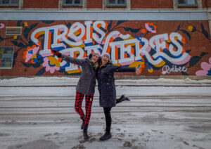 Girls getaway in Lanaudière-Mauricie, Authentic Quebec Trois-Rivières street art in winter, Kat and Lindsay posing in front of it wearing toques and jackets with big smiles