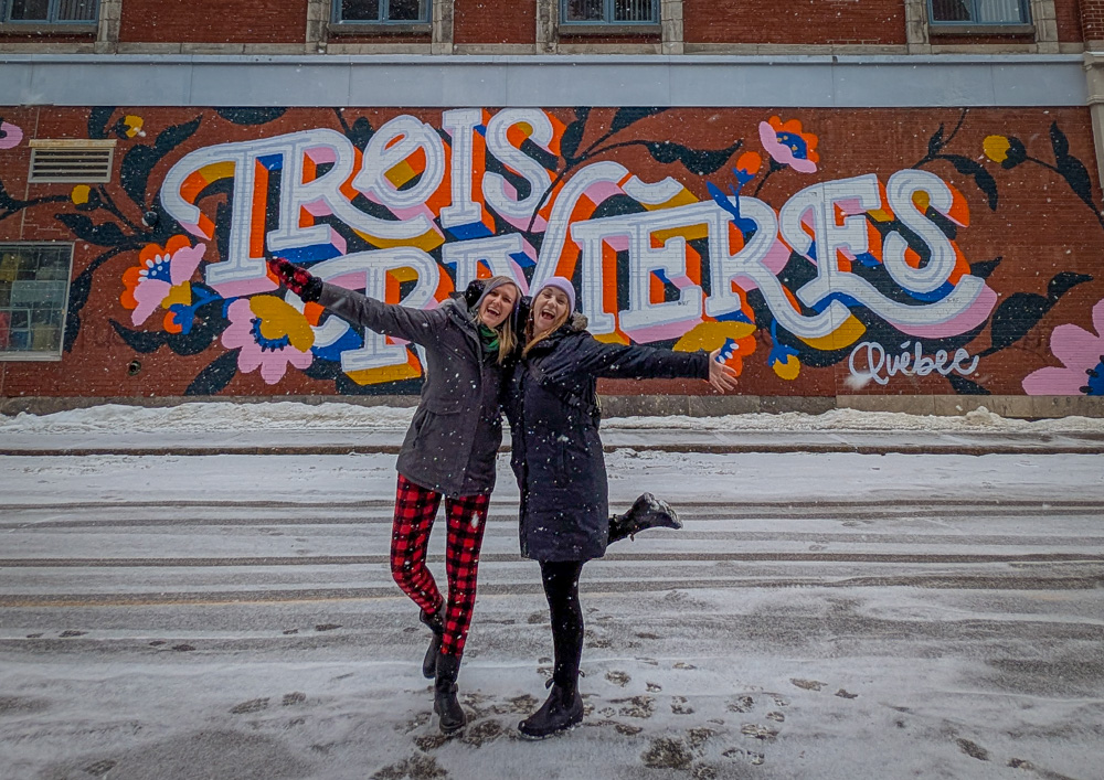 Girls getaway in Lanaudière-Mauricie, Authentic Quebec Trois-Rivières street art in winter, Kat and Lindsay posing in front of it wearing toques and jackets with big smiles